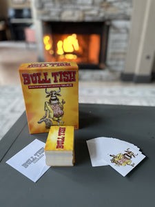 Bull Tish game with game pieces placed on a table. Cards from game say Bull Tish and show the dressed up smiling bull.