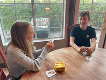 Two kids smiling and laughing while playing Bull Tish in a dining area.